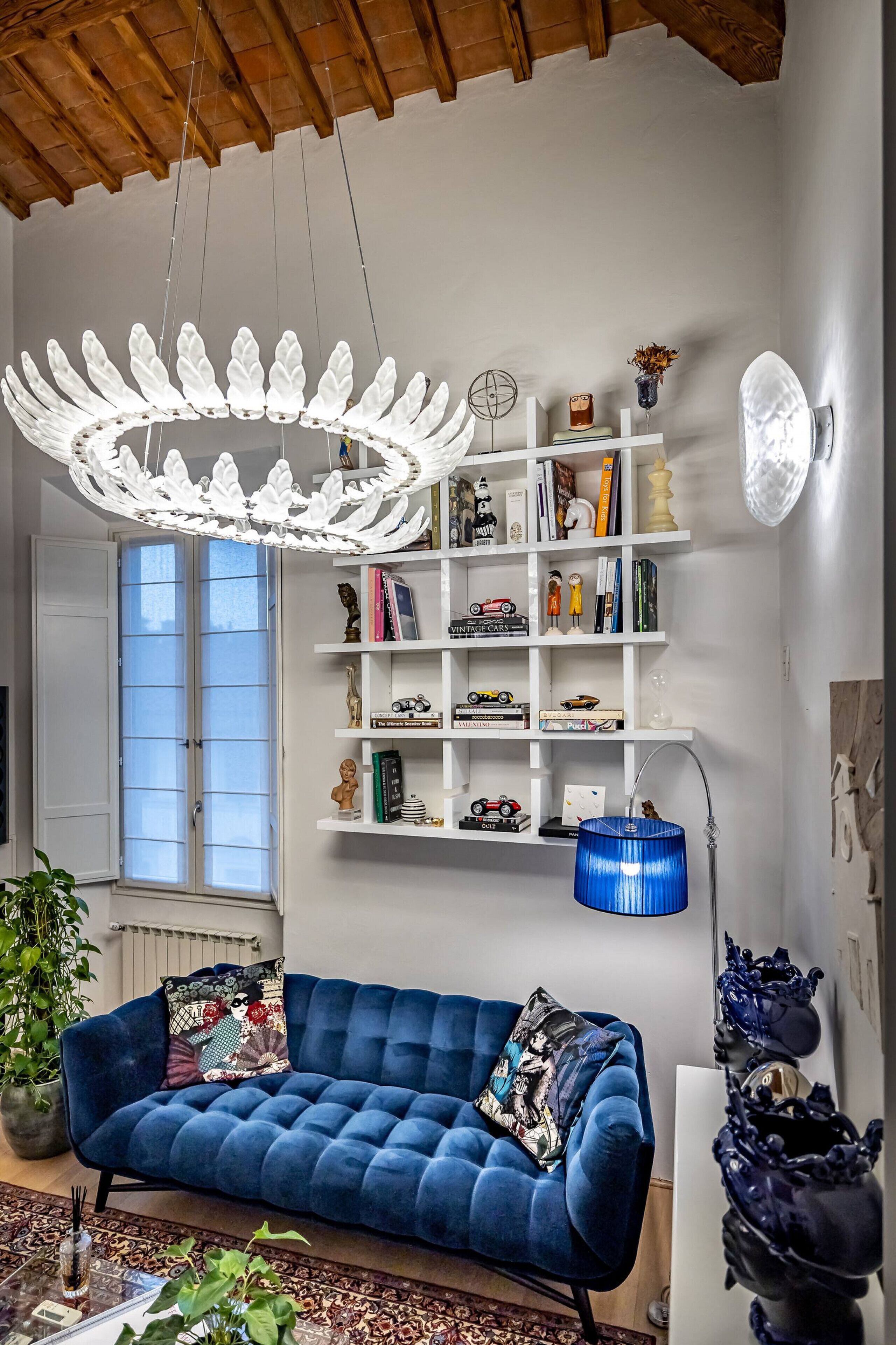 Un salon avec un canapé bleu, une bibliothèque blanche, une lampe bleue et un luminaire décoratif au plafond.