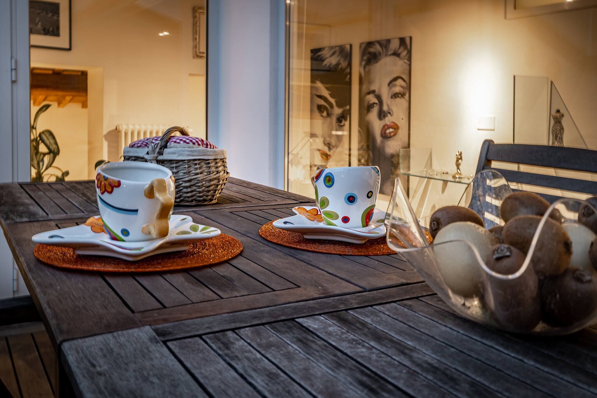 Una taula de menjador amb dues tasses blanques amb dibuixos colorits, una cistella de vimetla i un bol de vidre amb objectes decoratius.
