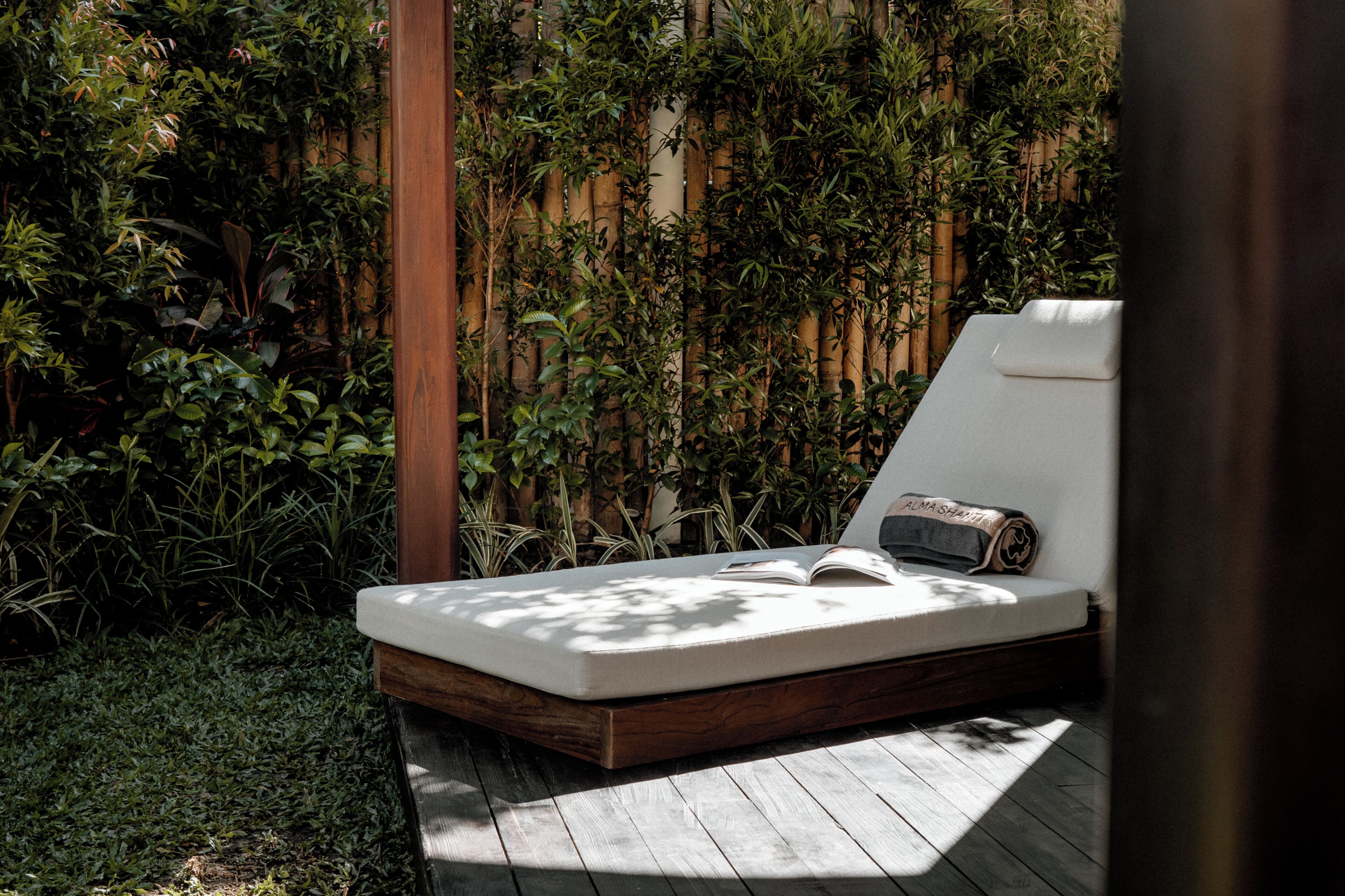 A wooden deck with a mattress and a pillow, surrounded by dense foliage.