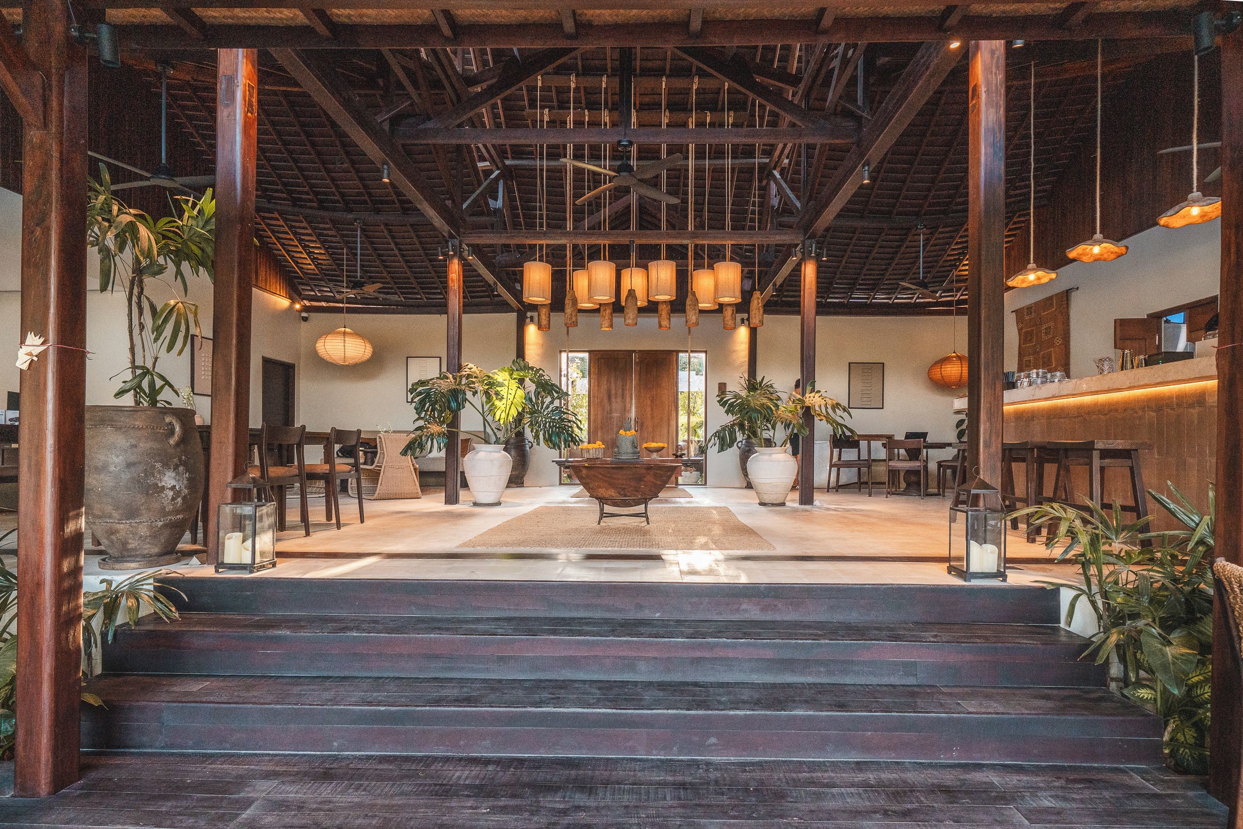 A spacious lobby with a central seating area, multiple potted plants, and a staircase leading to upper floors.