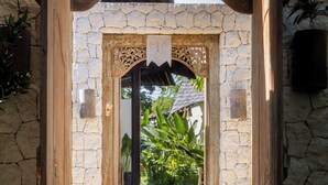 A stone archway leading to a courtyard with a wooden door and a stone wall.