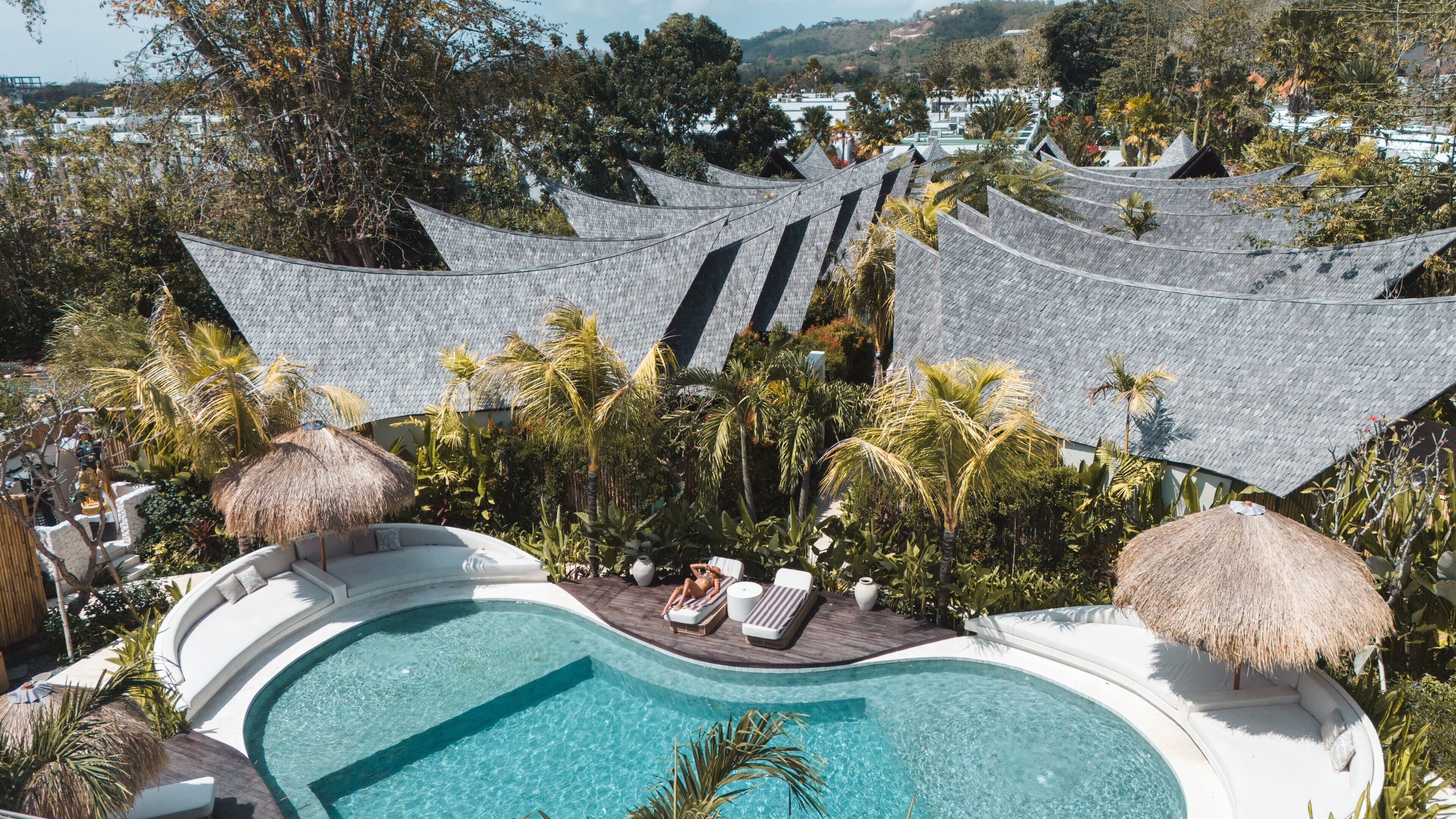 A pool area with lounge chairs and a thatched roof structure.