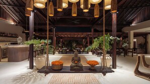 A lobby with a central Buddha statue, hanging pendant lights, and a bar area with bottles.