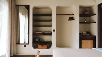 Una habitación con una cama, una ventana con cortinas, estantes empotrados, una cesta de mimbre y una pequeña estatua.
