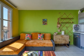 A room with a sofa, a small table, a kitchen area, and a window. - Apartment "Le Duplex Des Halles" with Balcony and Air Conditioning (Sète)