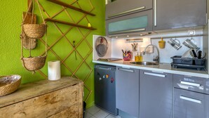 Eine Küche mit grüner Wand, Holzböden und Regalen, einem Geschirrspüler sowie diversen Küchenutensilien.