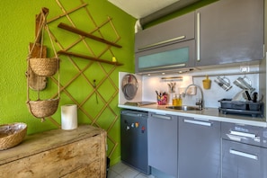 A kitchen with a green wall, wooden shelves, a dishwasher, and various kitchen utensils. - Apartment "Le Duplex Des Halles" with Balcony and Air Conditioning (Sète)