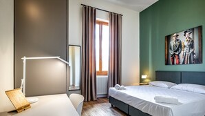 Una habitación de hotel con cama, mesita de noche, lámpara y un cuadro en la pared.