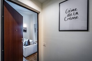 Un passadís amb una porta de fusta que dona a una habitació amb un llit i una placa a la paret.