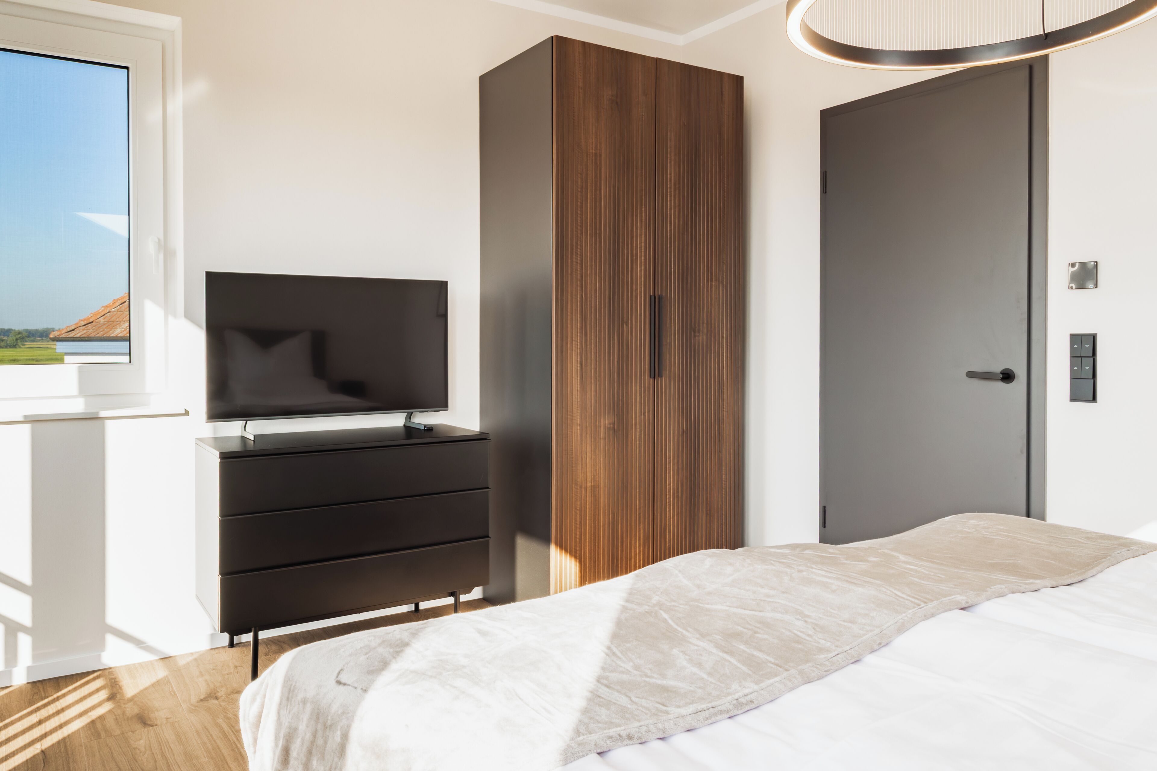 Une chambre à coucher avec un lit, un téléviseur posé sur une commode, une armoire et une porte.