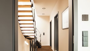 A modern interior with a wooden staircase, a hallway, and a door with a light switch. - ELBE.6 – Apartment II | 5-star right on the Elbe (Wittenberge)