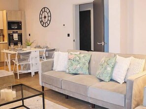 A living room with a sofa, a glass coffee table, a dining table with chairs, and a clock on the wall. - Effortless Stays at Luxury Birmingham 2BR Sleeps 6 (Deritend)