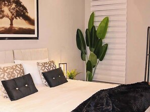 A bedroom with a bed, pillows, a plant, and a window with blinds. - Effortless Stays at Luxury Birmingham 2BR Sleeps 6 (Deritend)