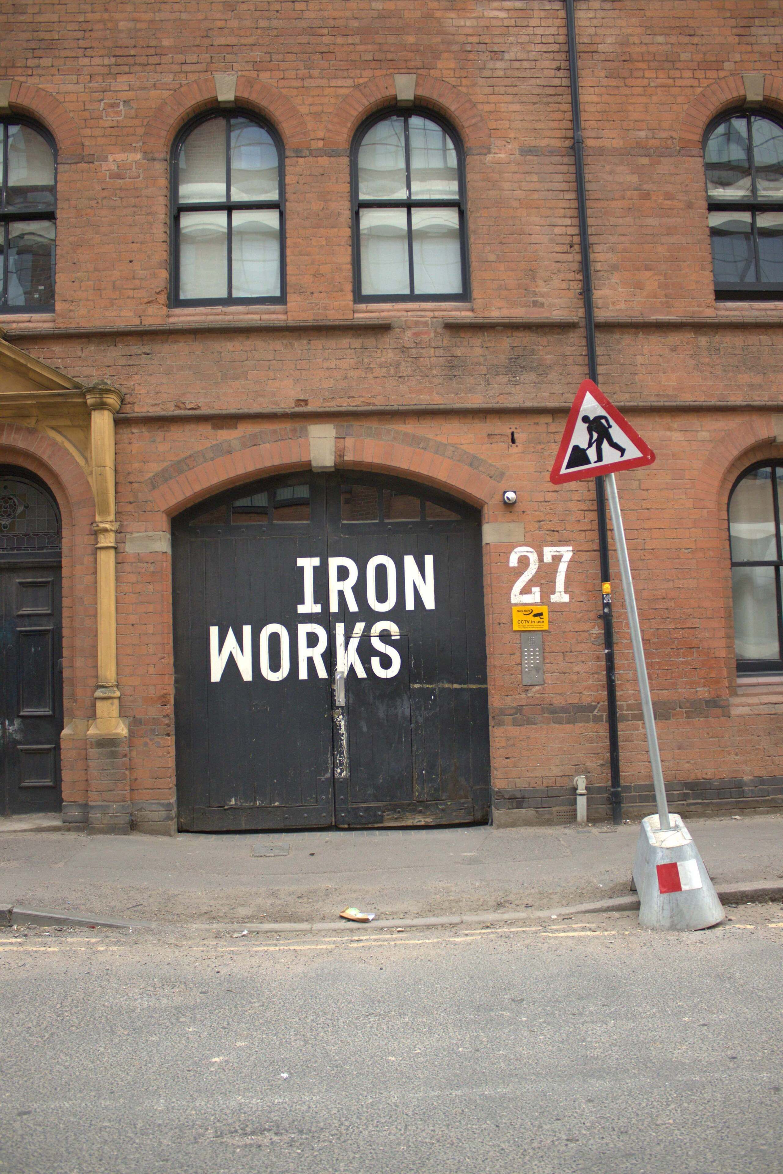 A brick building with a large black door labeled 'IRON WORKS 27' and a pedestrian crossing sign.