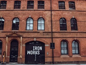 Punatiilinen rakennus, jossa on kaarevat ikkunat ja suuri musta ovi, jonka yläpuolella on teksti ’IRON WORKS’.