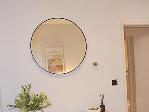 A room with a round mirror on the wall, a framed picture, a potted plant, and a small table with a decorative item. - Effortless Stays at Luxury Birmingham 2BR Sleeps 6 (Deritend)