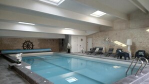 Una piscina interior con pared de piedra, una decoración de timón de barco y sillones de descanso.