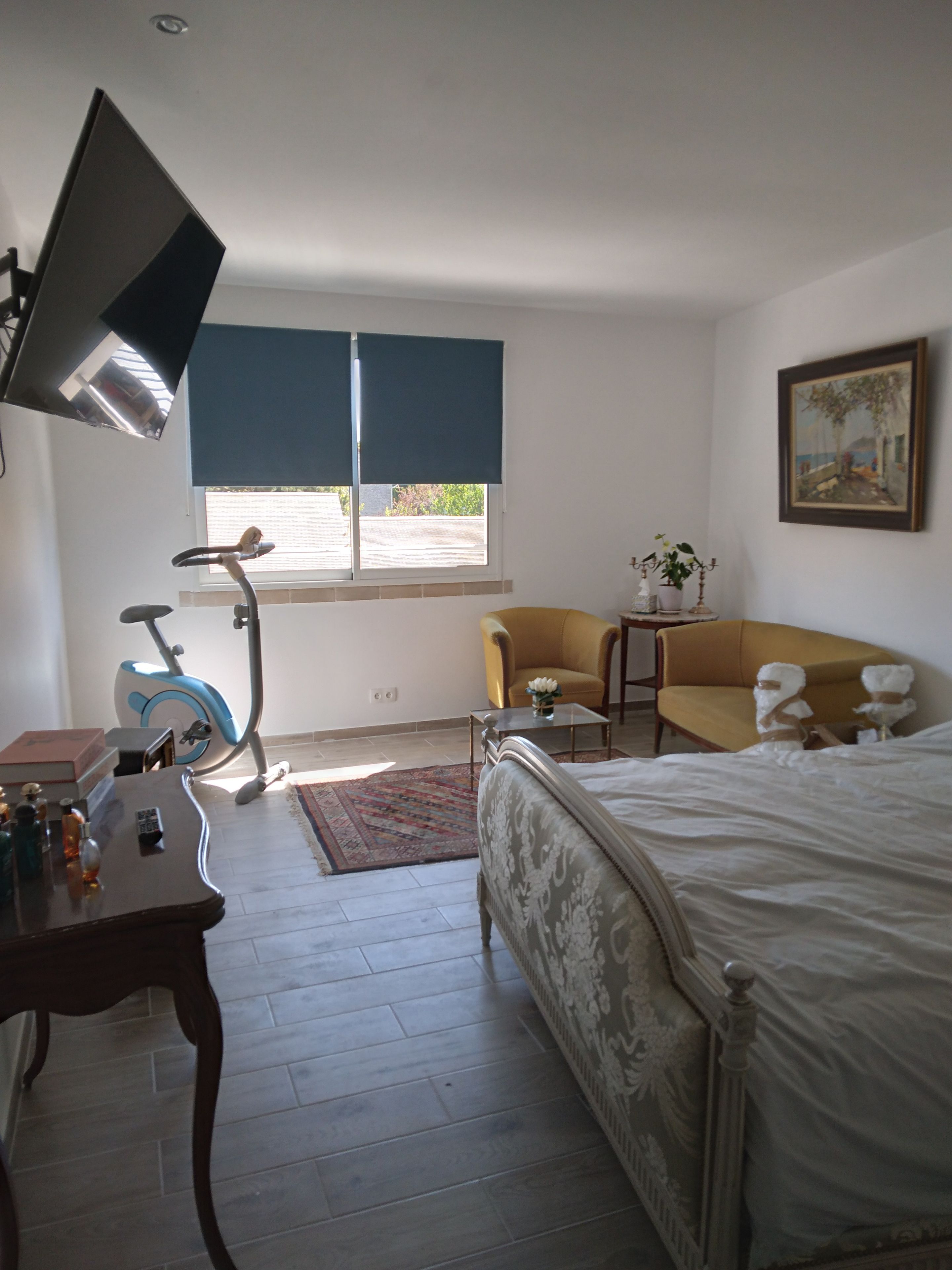 Un dormitorio con una cama, un escritorio con lámpara, una silla, una mesita con una planta y una ventana con persianas.