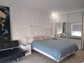 A bedroom with a bed, bedside tables, a bench, a mirror, and a textured wall.