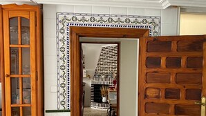 Un couloir avec une porte en bois, une armoire aux portes vitrées et un mur recouvert de carreaux, agrémenté d’une bordure décorative.