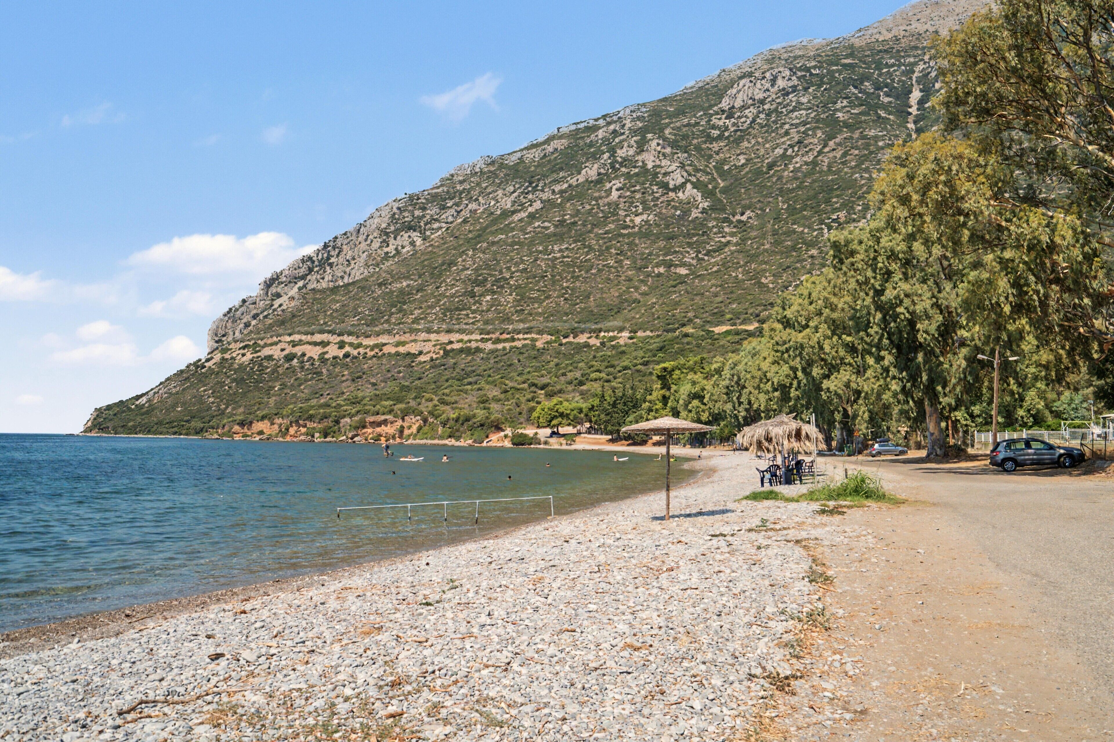 A pebble beach with a clear view of the sea and a mountain in the background.
