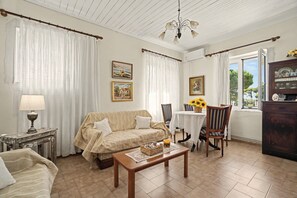 A cozy living room with a sofa, a table with a basket, a lamp, and a view of the outdoors through a window.