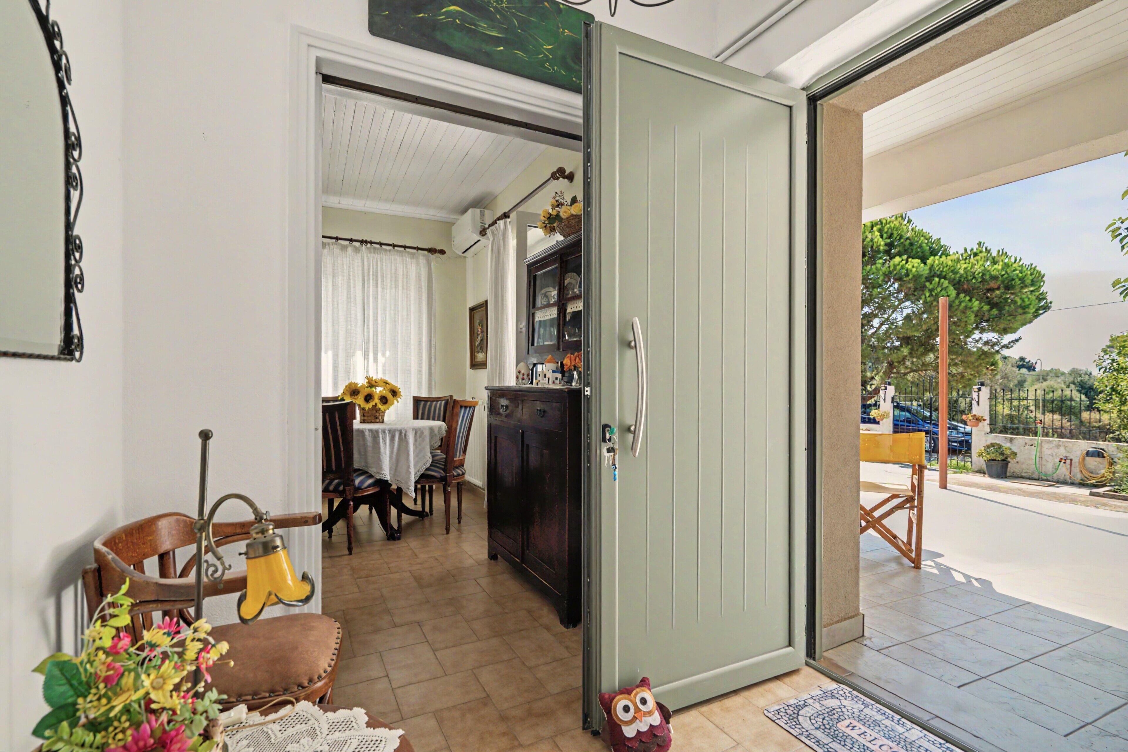 Una puerta abierta que da a un comedor con una mesa dispuesta para dos personas, un aparador de madera oscura y una pequeña decoración de un búho en el suelo.