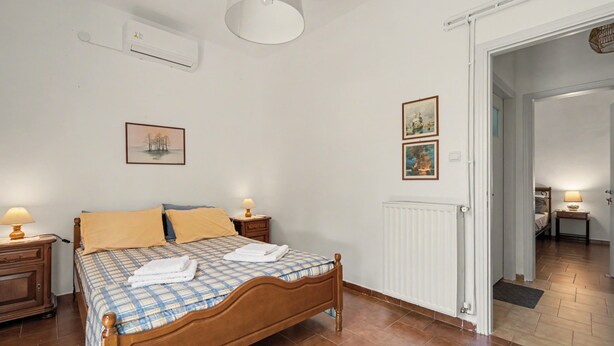 A bedroom with a wooden bed, two bedside tables with lamps, a radiator, and two framed pictures on the wall. - Nafpaktos The Home Country House with Sea View, Private Terrace & Air Conditioning (Agios Polykarpos)