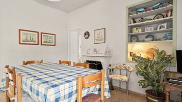 Un coin repas avec une nappe à carreaux, des chaises en bois, une cheminée et une bibliothèque agrémentée d’objets décoratifs.
