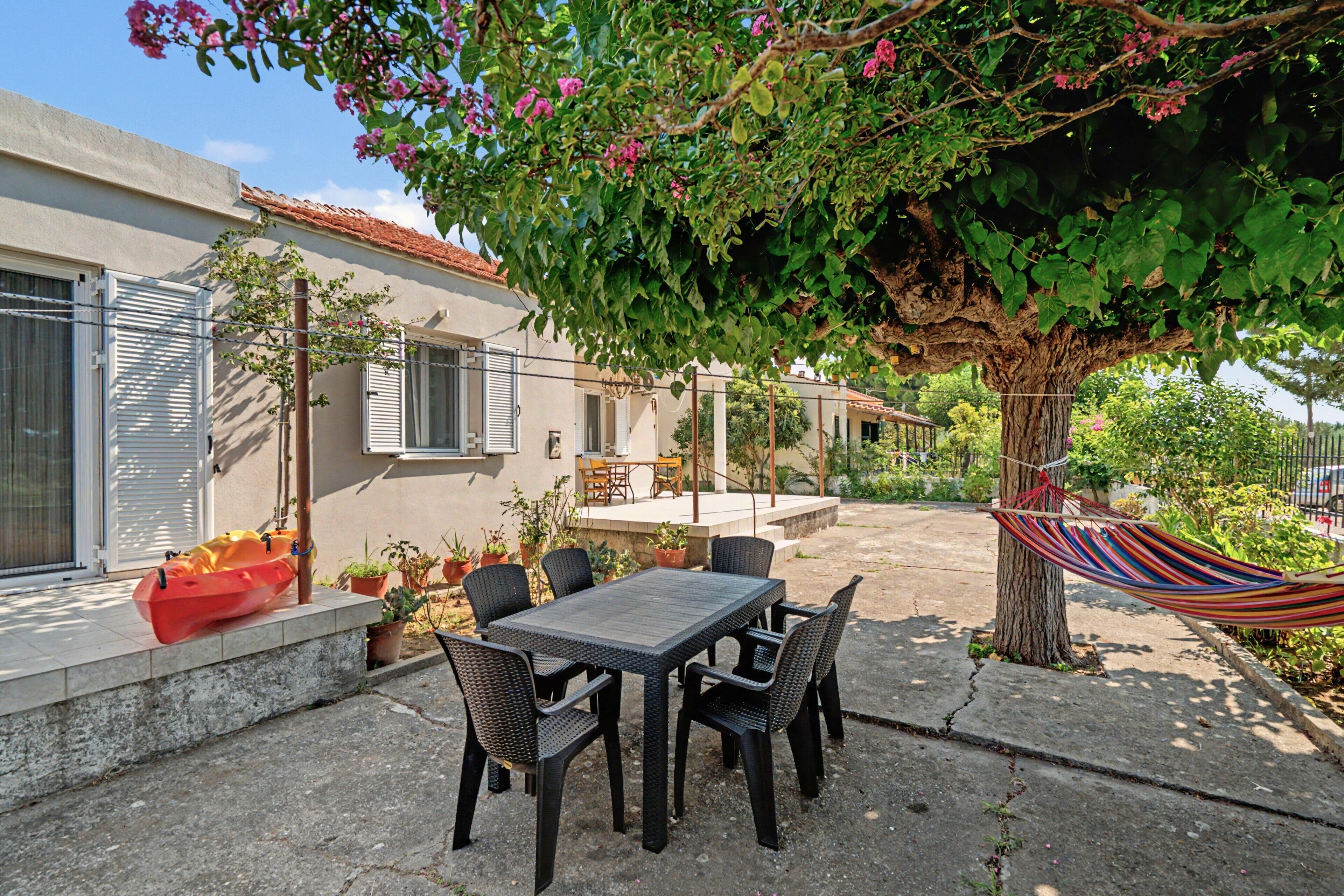 An outdoor patio with a table and chairs, a hammock, and a tree with pink flowers.
