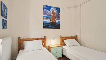 A bedroom with two beds, a nightstand with a lamp, and a painting of a ship on the wall.