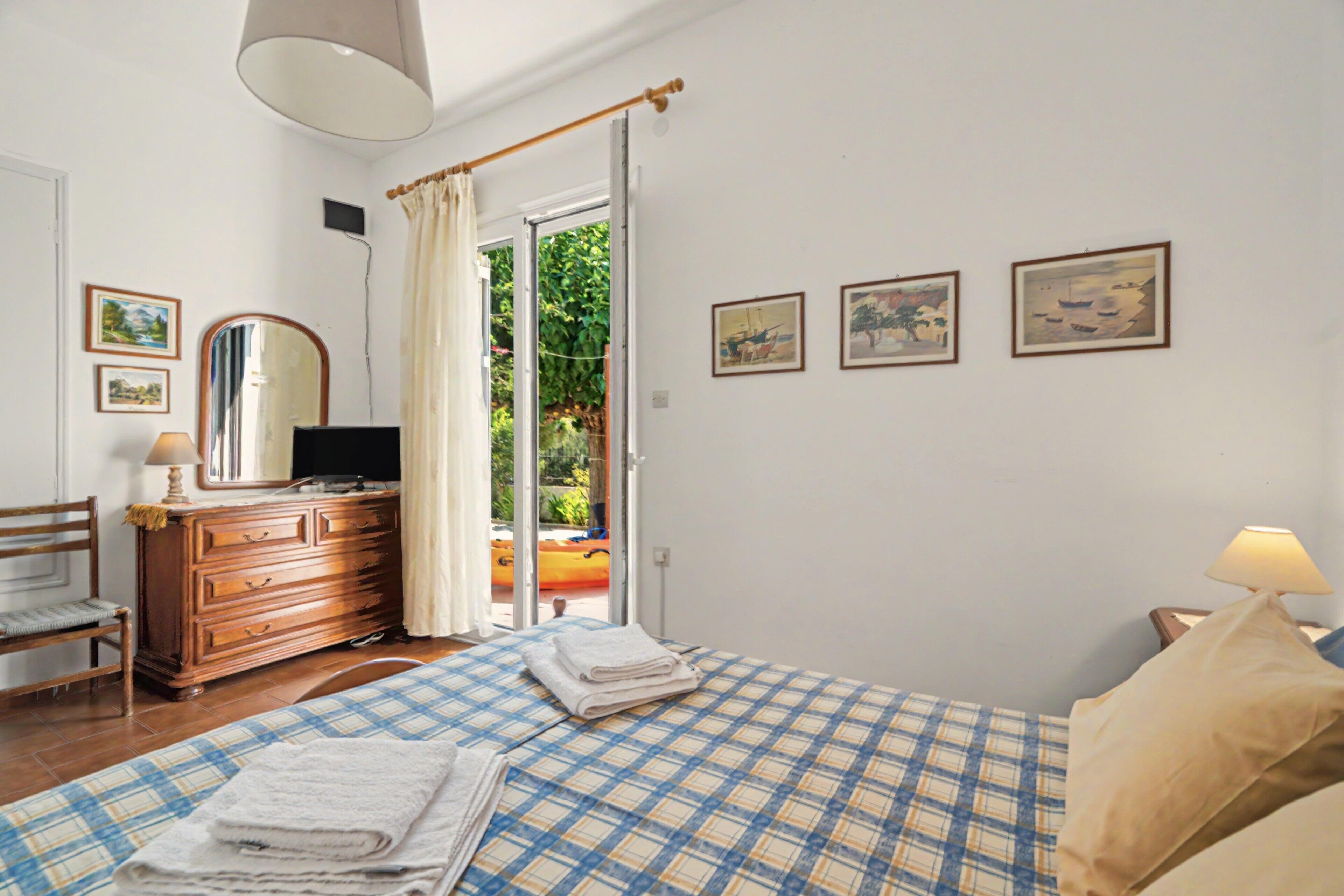 Una camera da letto con un letto, una cassettiera, una sedia, una televisione e una finestra con tende.
