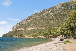 A beach with a rocky hillside, clear water, and a few people swimming.