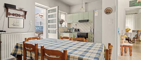Uma sala de jantar com toalha quadriculada, cadeiras de madeira e vista para a cozinha.