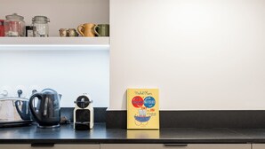 Une cuisine équipée d’une bouilloire, d’une machine à café et d’une boîte jaune posée sur le plan de travail.