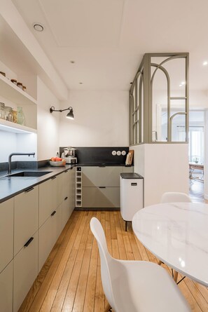 A modern kitchen with a black countertop, white cabinets, and a wooden floor. - Avenue Foch Retreat, by Veeve (Paris)