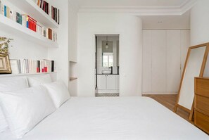 A bedroom with a large bed, a bookshelf, a wardrobe, and a view into the bathroom. - Avenue Foch Retreat, by Veeve (Paris)