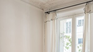 Une pièce chaleureuse avec un canapé marron foncé, une table ronde blanche sur laquelle se trouvent un livre et une bougie, un lampadaire et une fenêtre avec des rideaux.