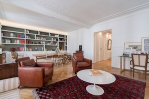 A spacious living room with leather sofas, a round coffee table, a large bookshelf, and a dining area with a table and chairs. - Avenue Foch Retreat, by Veeve (Paris)