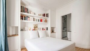 Une chambre à coucher avec un grand lit, une bibliothèque, une armoire et une salle de bain visible à travers une porte ouverte.