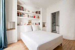 Ein Schlafzimmer mit einem großen Bett, einem Bücherregal, einem Kleiderschrank und einem durchgegangenen Tür sichtbaren Badezimmer.
