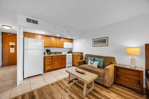 A compact living space with a kitchenette, a sofa, a coffee table, and a lamp. - West Maui Studio with Ocean Views & Resort Amenities -Royal Kahana 204 (Lahaina)