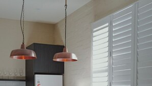 Eine moderne Küche mit einer zentralen Kochinsel, einem Esstisch mit Stühlen und einem Fenster mit Jalousien.