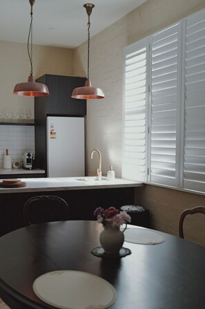 A modern kitchen with a central island, a dining table with chairs, and a window with blinds. - The Fable Fitzroy Melbourne (With Parking) (Fitzroy)