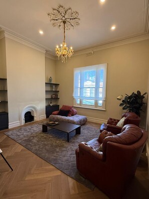 A spacious living room with a fireplace, a large window, and a chandelier. - The Fable Fitzroy Melbourne (With Parking) (Fitzroy)