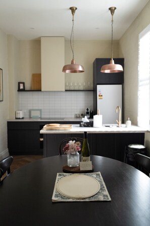 A modern kitchen with pendant lighting, a dining table set for two, and a refrigerator. - The Fable Fitzroy Melbourne (With Parking) (Fitzroy)