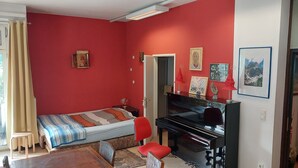 A bedroom with a bed, a desk with a computer, a piano, and a red wall. - 1-room apartment with a balcony (Graz)