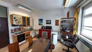 A compact kitchen with a microwave, oven, and sink. There is a dining table with chairs, a bookshelf, and a statue on a shelf. - 1-room apartment with a balcony (Graz)
