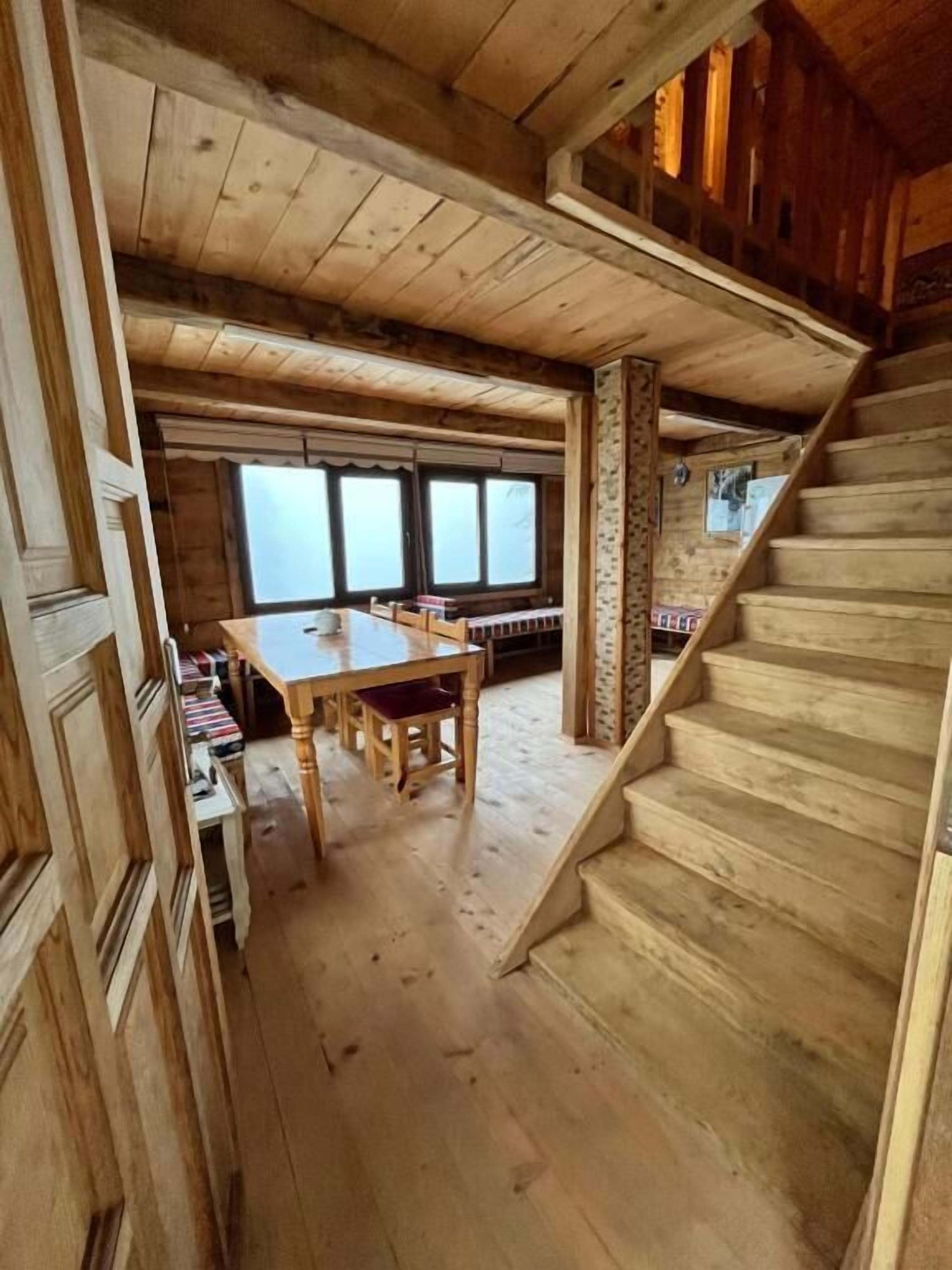 A wooden interior with a staircase, a dining area, and a view through large windows.