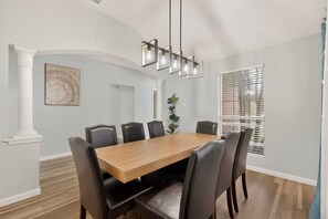 A dining room with a wooden table and chairs, a hanging light fixture, a plant, and a window with blinds. - Modern Mesquite Retreat  Patio + Smart TVs (Mesquite)
